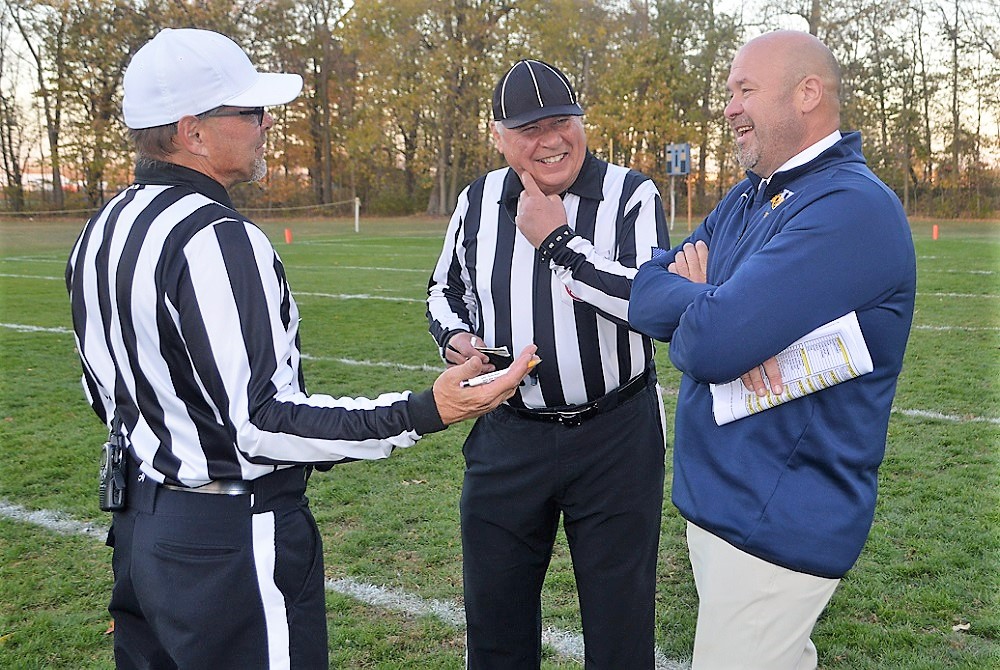 Retiring official Tom Crampton, middle, shares a laugh with referee colleague Chris Dauterman and Whiteford varsity football coach Todd Thieken before Crampton’s final game Friday. 