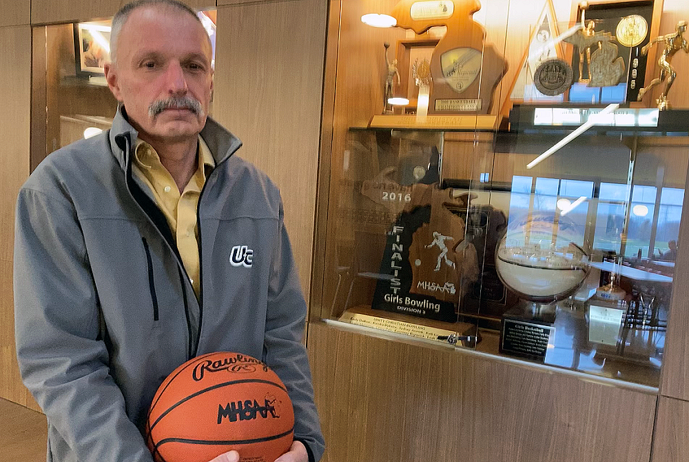 Hudsonville Unity Christian boys basketball coach Scott Soodsma stands in front of a portion of the school’s trophy case, which he’s helped fill over decades coaching basketball. 