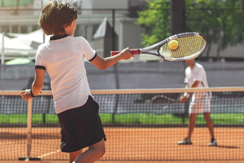 A child playing tennis connects with the ball.