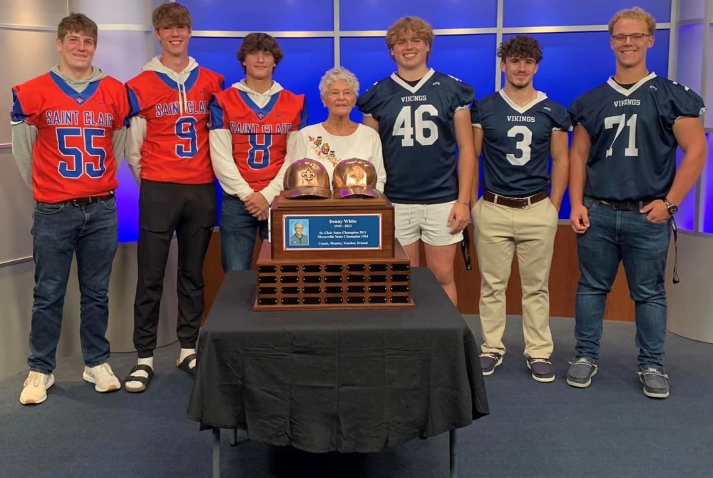 From left: St. Clair’s Larry Wawryzniak, Liam Nesbitt and Peyton Ellis, Denny White’s wife Karen White, and Marysville’s Bryce Smith, Carter Saccucci and Caz Carty stand with the first-year traveling trophy celebrating Denny White’s coaching career.