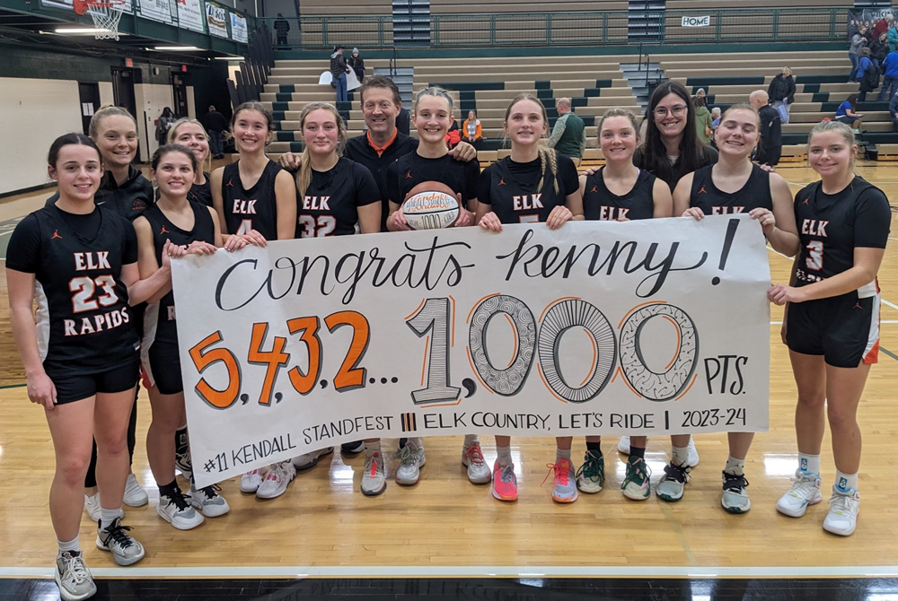 The Elk Rapids girls basketball team celebrates Kendall Standfest’s 1,000th career point; she’s holding the basketball. 