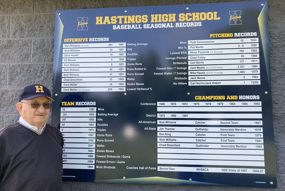 Retired Hastings baseball coach Bernie Oom stands with the record board he’s created that is displayed at the school’s diamond.