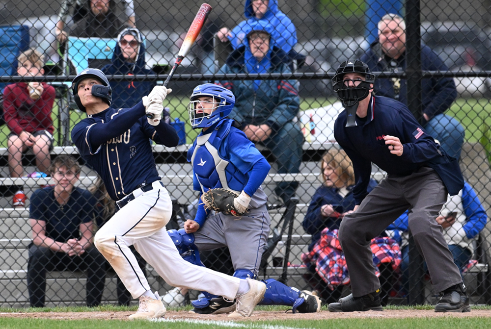 A baseball hitter, catcher and umpire watch a fly ball soar into the air.