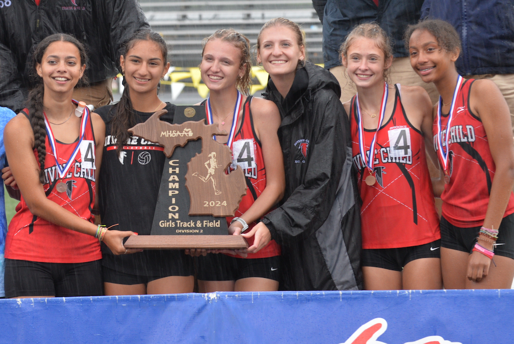 Members of Dearborn Divine Child’s girls track & field team hold up their latest championship trophy Saturday.