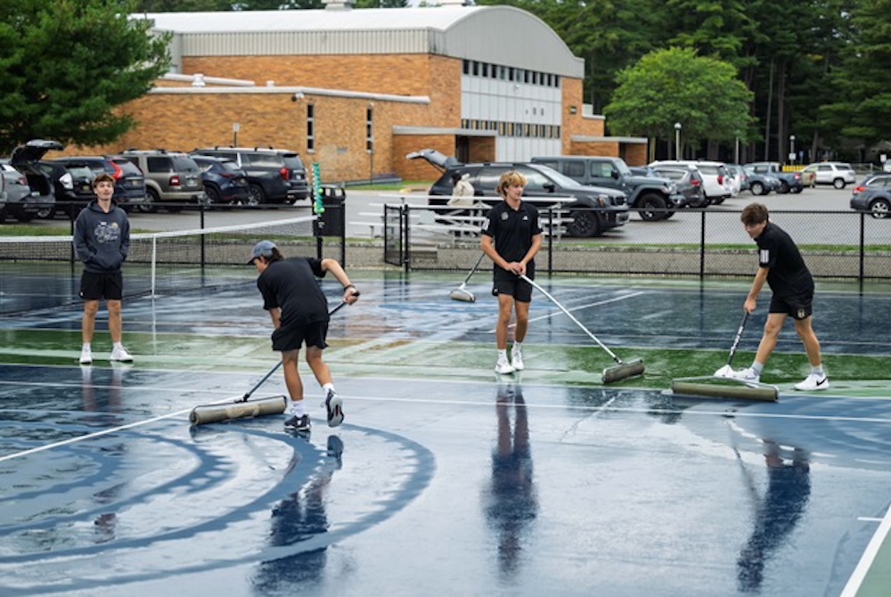 Traverse City Central tennis players clear water from the Larry Nykerk Trojan Tennis Center courts this fall.