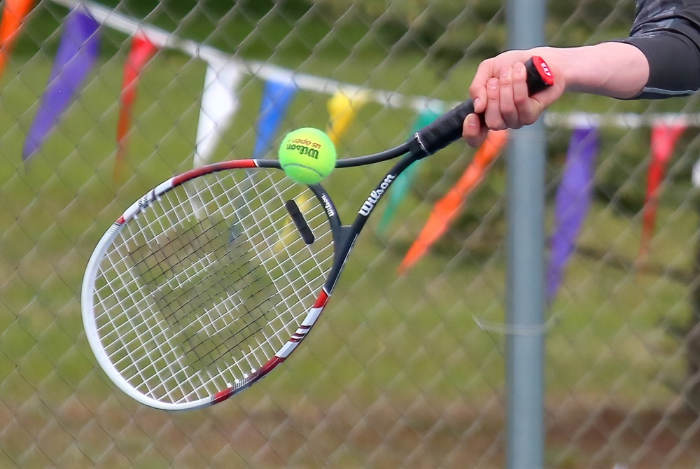 A tennis racket is swung toward a tennis ball. 
