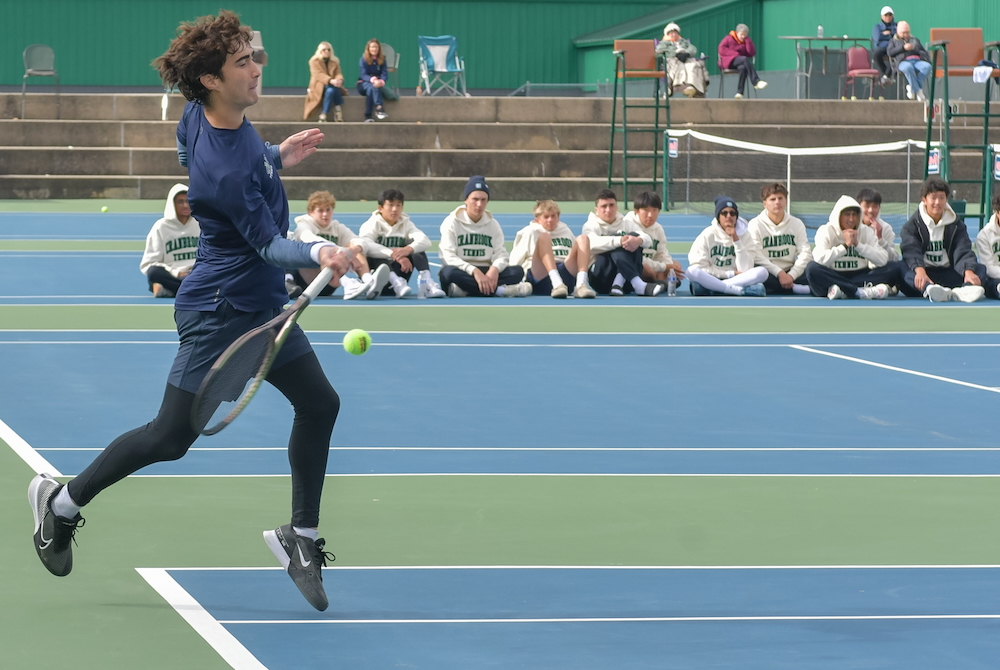A Cranbrook tennis player hits a forehand while his team cheers him on.