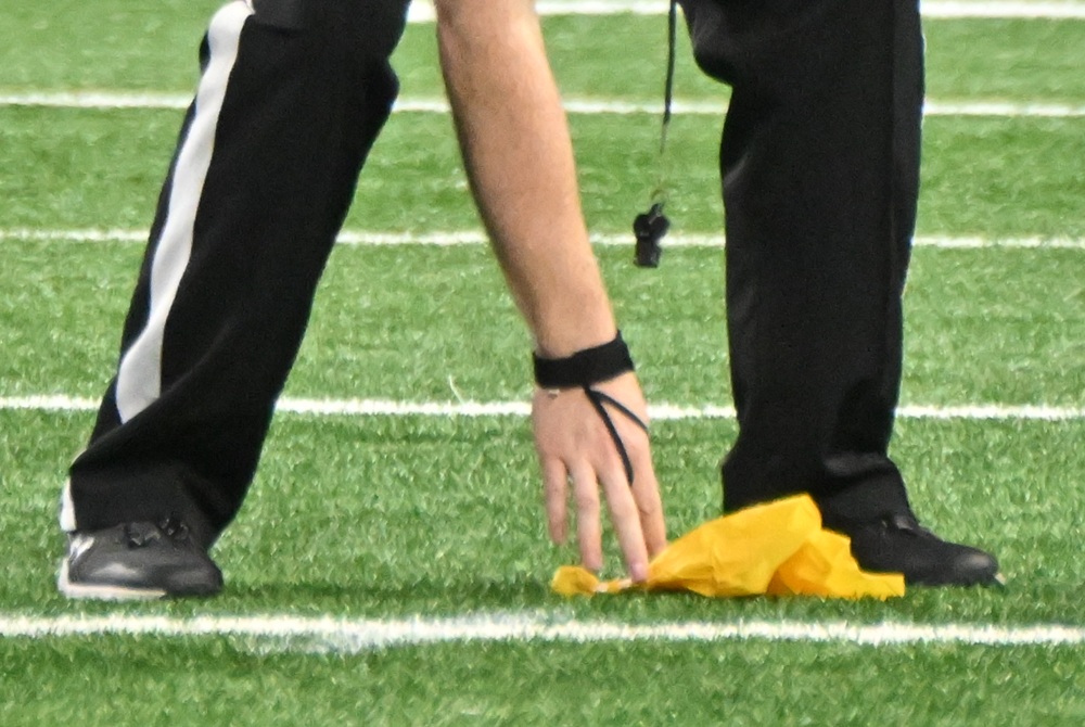 A football official picks a penalty flag up off the turf.