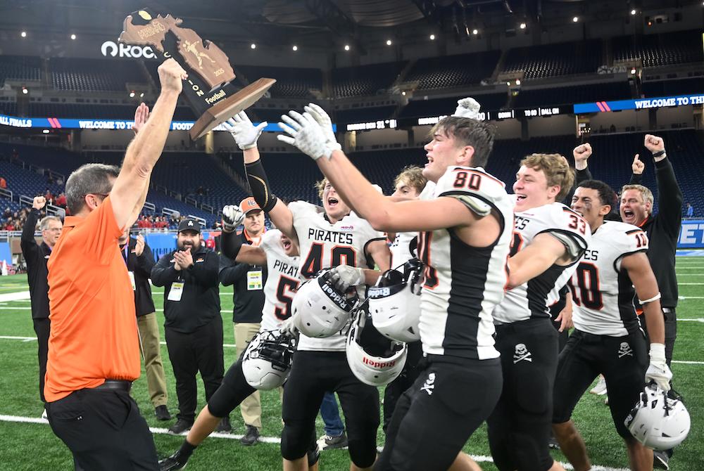 Harbor Beach coach Troy Schelke hands off his team’s championship trophy to his players Friday at Ford Field.