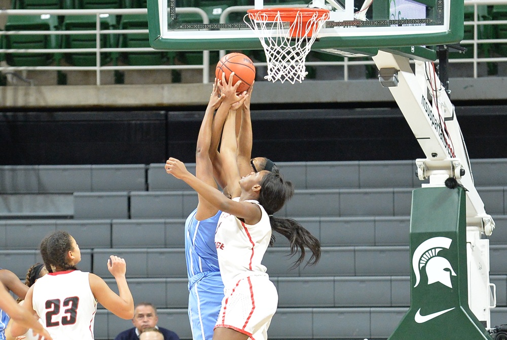 Three players attempt to grab a rebound during a 2017 basketball game.