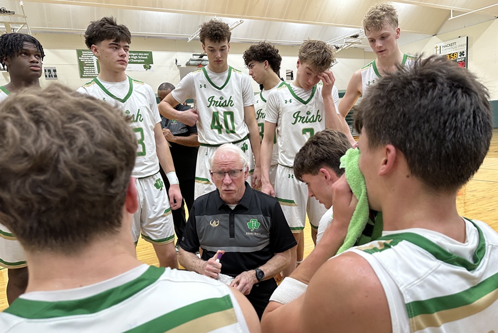 Hackett Catholic Prep boys basketball head coach Dan Hoff, kneeling, talks with his players during a break this season. 