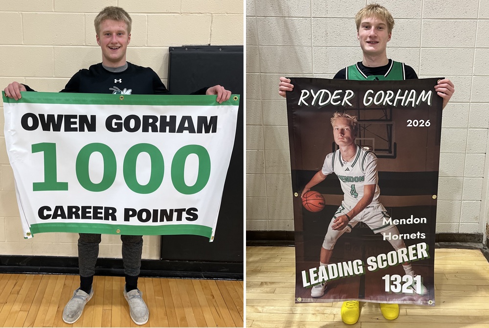 At left, Owen Gorham shows off a banner earlier this season identifying him as a 1,000-point scorer. At right, Ryder Gorham holds up a banner commemorating him as Mendon's all-time leading scorer with 1,344 points following Monday's 84-40 win at Bellevue.