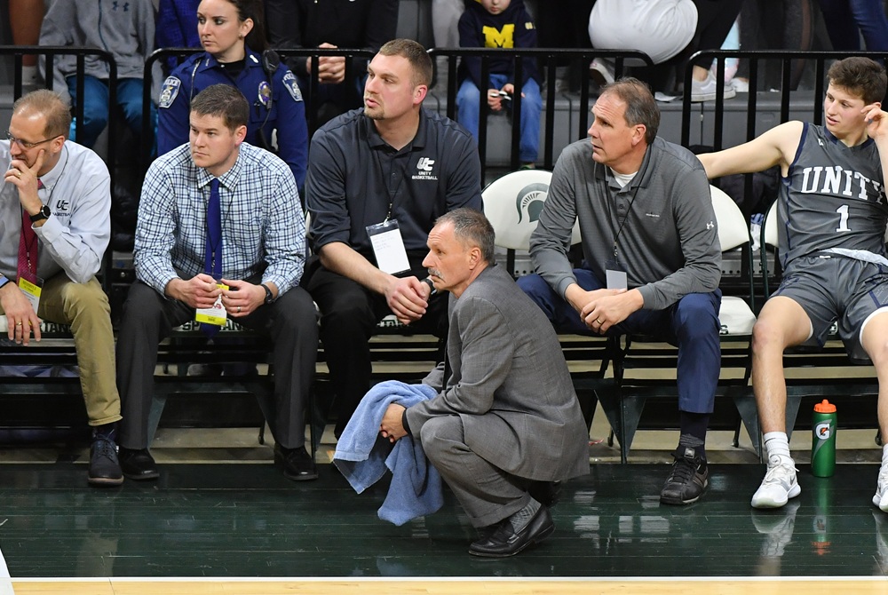 Unity Christian boys basketball coach Scott Soodsma, kneeling, confers with his staff during his team’s 2019 Division 2 Boys Semifinal win over Ludington. 