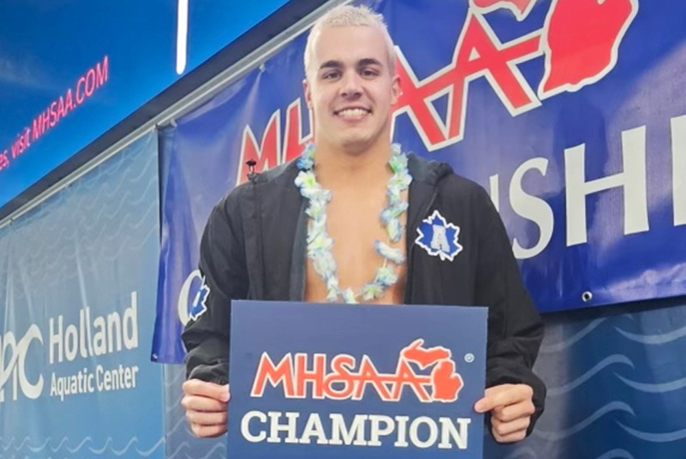 Adrian’s Kade Opsal stands on the medal podium after winning the 100-yard backstroke at the Lower Peninsula Division 3 Finals in Holland.