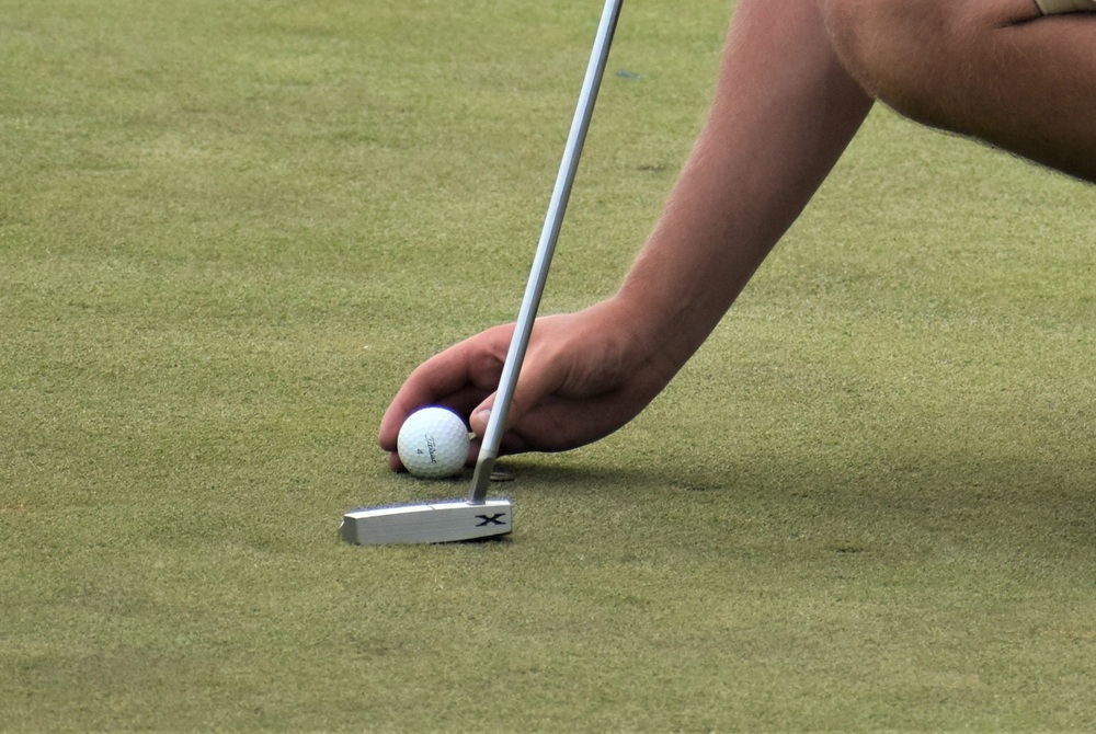 A golfer places a golf ball on the green. 