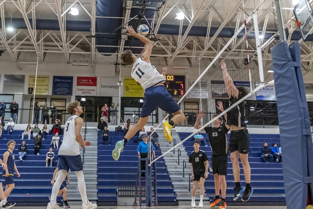 A volleyball player gets high over the net in mid-swing during a match.