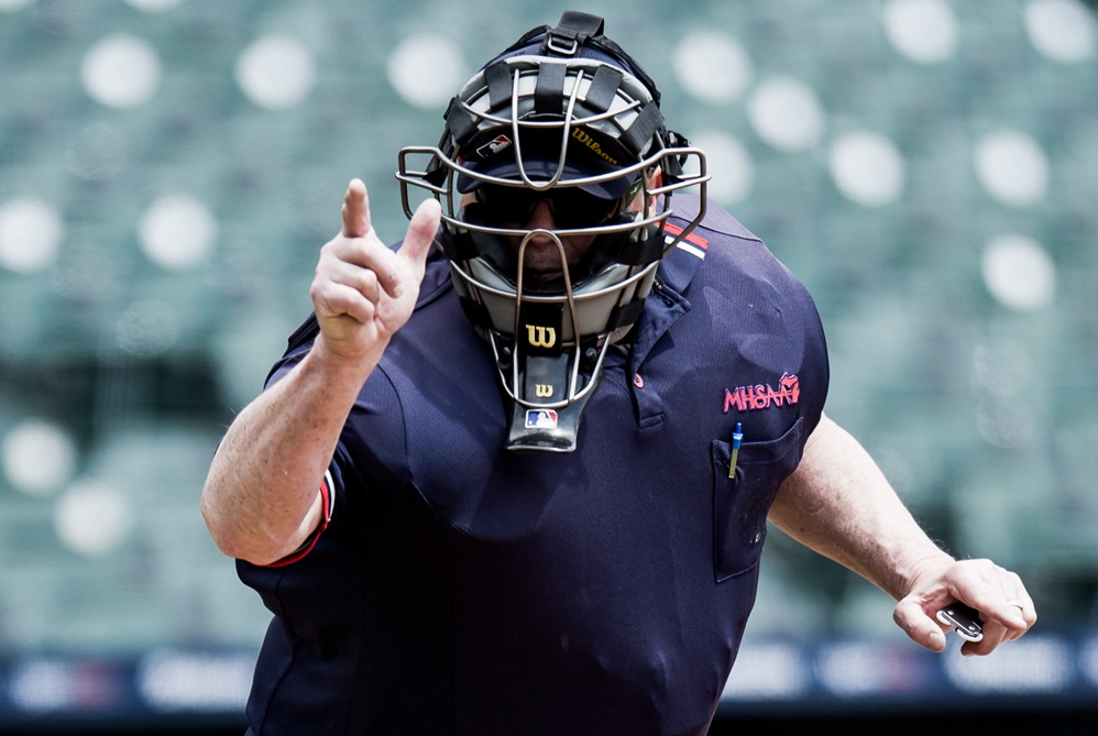 A baseball umpire signals a strike by pointing to his right. 