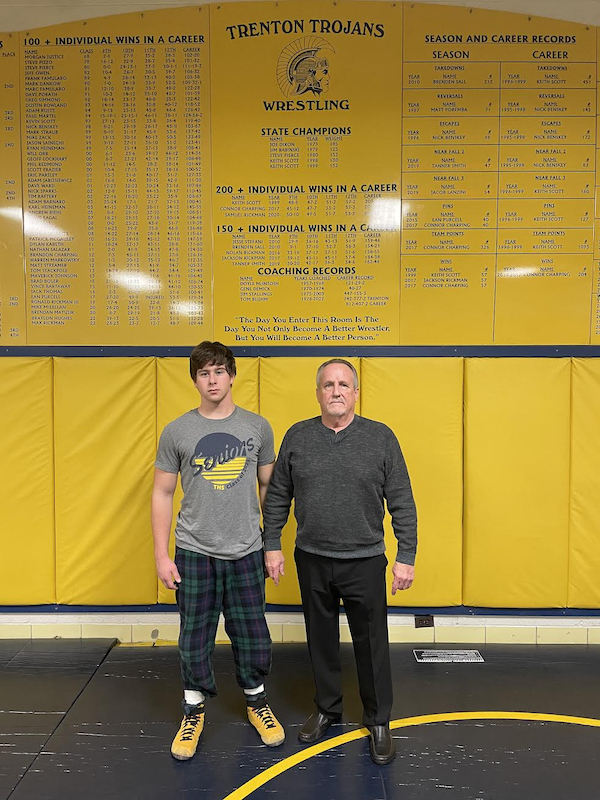 Bluhm and current wrestler Nolan Diroff stand in front of the program's record board.