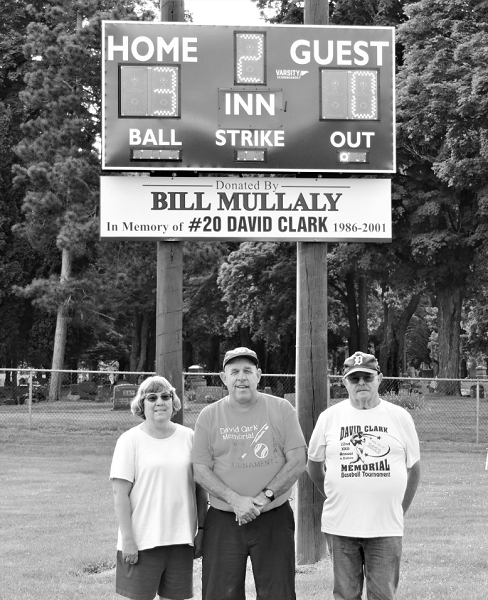 Mullaly, middle, stands last July with Jo Ann and Watson Clark in front of a scoreboard he donated to Will Carleton Park; the photo was taken during the 22nd David Clark Memorial Baseball Tournament. 