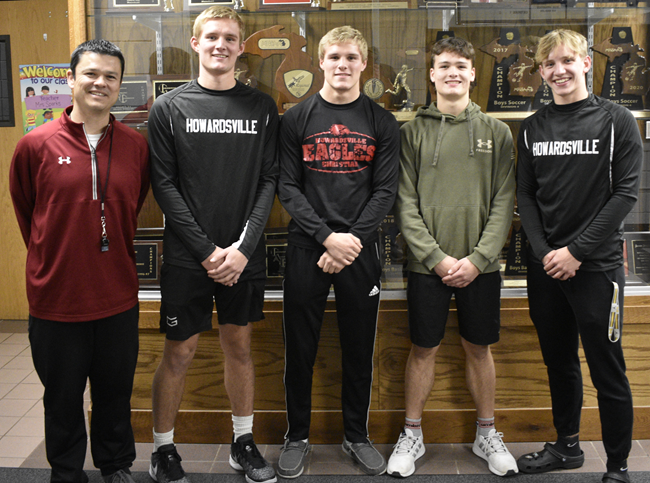 Eagles varsity boys basketball coach Ken Sparks, far left, is pictured by the school's trophy case with his four returning starters Colin Muldoon, Dylan Muldoon, Kaden Sparks and John Paul Rose. 