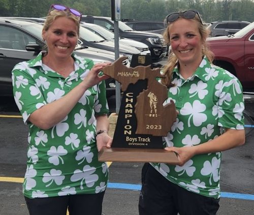 Hackett track coaches Charissa Dean, left, and Shelly Germinder hold up last season’s MHSAA Finals championship trophy.