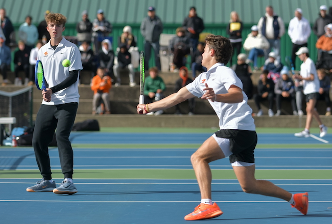 A Byron Center doubles player hits a forehand while his partner plays the net.