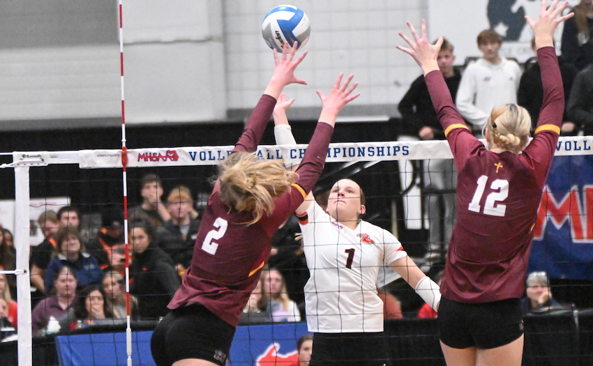 Byron Center junior Caitlin Hartson (1) attempts to get a kill over the Mercy block of Kalczynski and sophomore McKenzie Andrews (12).