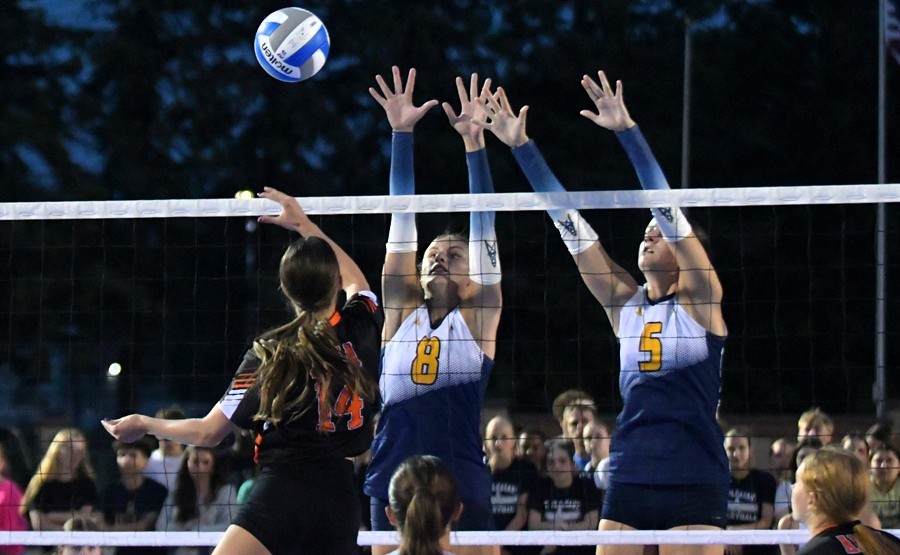 A pair of Mount Pleasant blockers rise above the net during an outdoor match against Alma this fall.